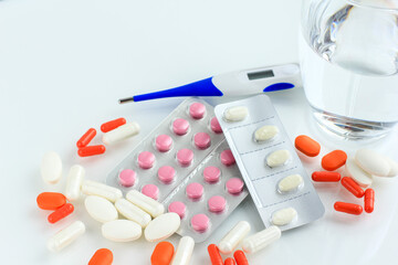Multicolored pills, tablets against the virus, flu, disease, a thermometer and a syringe on light...