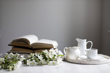 A branch of a blossoming apple tree or cherry on an open book and cup of coffee on a background of a blue wall. Concept - online learning. Copy space. Education on-line