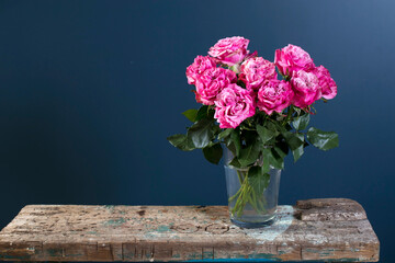 Bouquet of red roses in a glass vase on a dark blue background on a wooden wrecked surface of the bench.