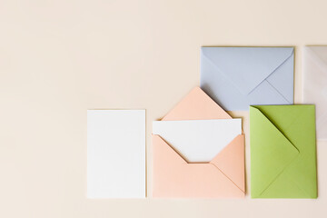 Mockup blank letter inside pink envelope, empty white paper and colorful closed envelopes on beige background, top view. Greeting card concept with copy space. Universally invitation template