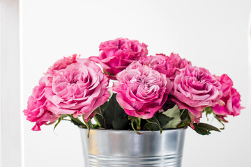 Bouquet of red roses in a tin bucket on a white wall background.