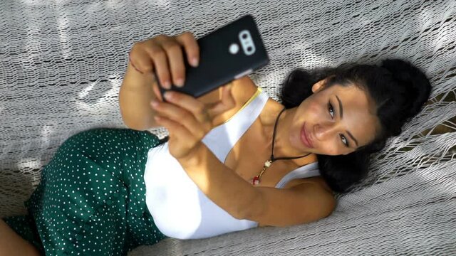 Young happy asian woman taking selfie photo with cellphone lying on hammock