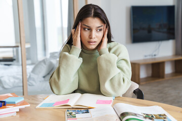 Photo of woman with headache rubbing her temples while doing homework