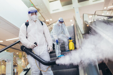 Professional workers in hazmat suits disinfecting indoor of mall, pandemic health risk, coronavirus - obrazy, fototapety, plakaty