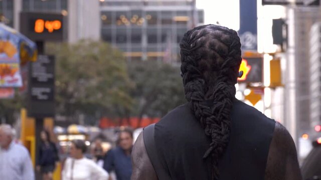 Afroamerican black man with long dreadlocks hair walking and listening to music in slow motion in New York City, Manhattan, with the radio city music hall in the background.