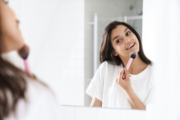 Photo of woman smiling and using powder brush while looking at mirror