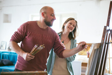 A man teaches a woman to paint a picture. Drawing lesson workshop in the studio. Teacher and student. Positive atmosphere of happiness smiles. mental health. Recreation   Middle aged couple love