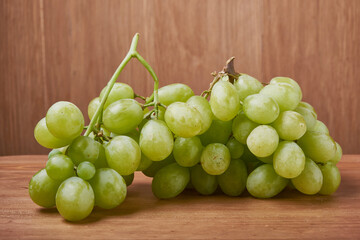 A bouquet of green grapes in a basket, autumn fruits, a symbol of abundance on a rustic background of a tree with a copy space, close-up.