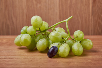A bouquet of green grapes in a basket, autumn fruits, a symbol of abundance on a rustic background of a tree with a copy space, close-up.
