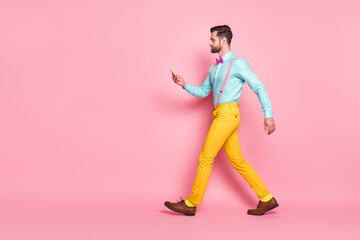 Fototapeta na wymiar Full size profile side photo of serious focused guy blogger go walk copyspace use cellphone read social network news post wear trousers shoes shirt isolated pastel color background