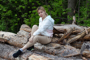 Outdoor close up portrait of young beautiful woman coat,sitting on a tree stump, Trees Chopped And Stacked In Forest