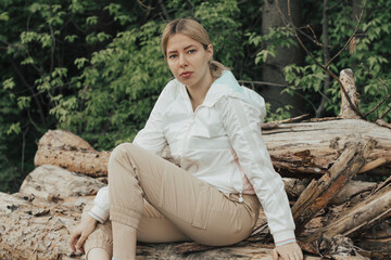 Outdoor close up portrait of young beautiful woman coat,sitting on a tree stump, Trees Chopped And Stacked In Forest