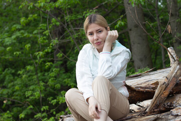 Outdoor close up portrait of young beautiful woman coat,sitting on a tree stump, Trees Chopped And Stacked In Forest
