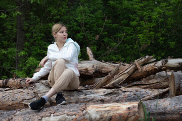 Outdoor close up portrait of young beautiful woman coat,sitting on a tree stump, Trees Chopped And Stacked In Forest