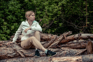 Outdoor close up portrait of young beautiful woman coat,sitting on a tree stump, Trees Chopped And Stacked In Forest