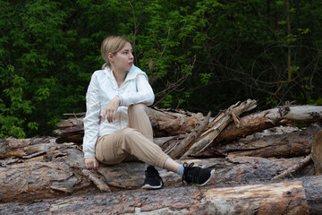 Outdoor close up portrait of young beautiful woman coat,sitting on a tree stump, Trees Chopped And Stacked In Forest