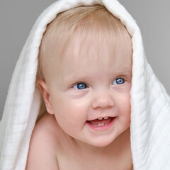 Cute little baby at home in bed covered with white blanket. Beautiful smiling cute baby girl.