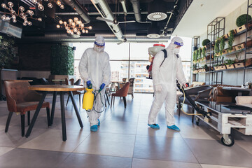 Obraz premium Professional workers in hazmat suits disinfecting indoor of cafe or restaurant, pandemic health risk, coronavirus