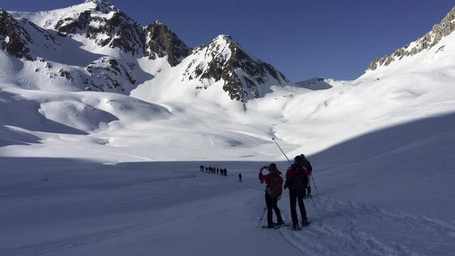 Some hikers go on snowshoes through an enchanting snowy Swiss Alpine valley near the Lukmanier pass.