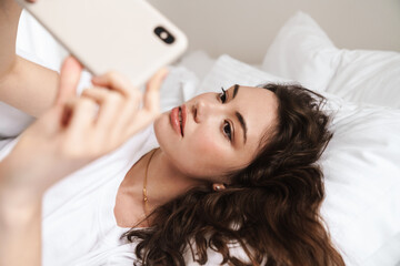 Obraz na płótnie Canvas Photo of attractive woman taking selfie on cellphone while lying on bed