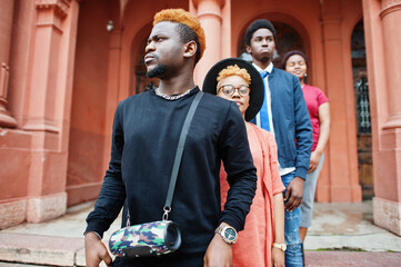 Four african friends posed outdoors against old architecture. Two black girls with guys.