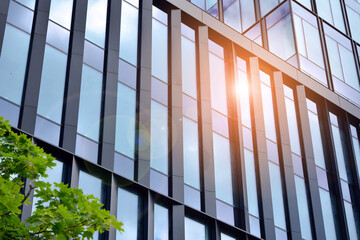 Facade texture of a glass mirrored office building. Fragment of the facade. Bottom view of modern skyscrapers in business district in evening light at sunset with lens flare filter effect.