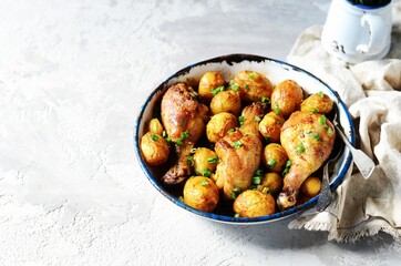 Baked chicken legs with young potatoes in a baking dish on a gray background