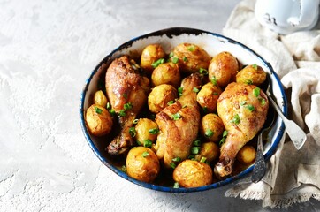 Baked chicken legs with young potatoes in a baking dish on a gray background