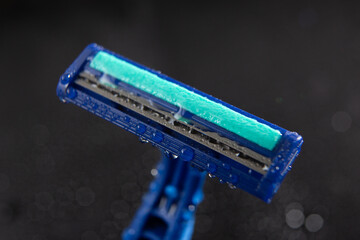 blue disposable razor blade, on black background with water drops