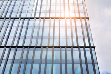 Facade texture of a glass mirrored office building. Fragment of the facade. Bottom view of modern skyscrapers in business district in evening light at sunset with lens flare filter effect.