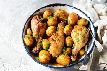 Baked chicken legs with young potatoes in a baking dish on a gray background