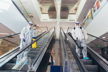 Professional workers in hazmat suits disinfecting indoor of mall, pandemic health risk, coronavirus