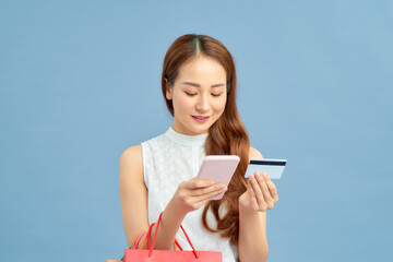 Stylish woman with shopping bag, credit card and phone on the blue wall background