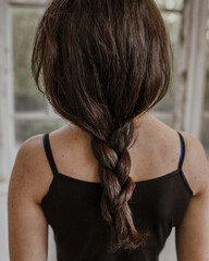 Fototapeta na wymiar A girl with a braid in a black dress is standing with her back