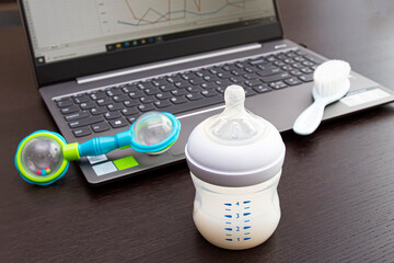 work computer with baby bottle, pacifier and rattle on the table