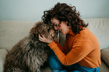 .Young curly short hair woman playing with her faithful spanish water dog at home. Affection and friendship. Lifestyle