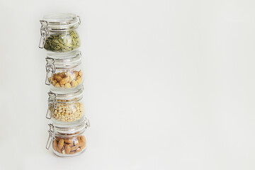different types of nuts in glass jars stand one on one tower on a white background