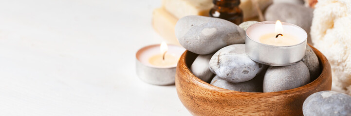 Fototapeta na wymiar Spa composition with essential oil, stones, soft towel, candle. Aromatherapy and relax, atmosphere of serenity and relaxation. Close up, macro. White wooden background, copy space for text. Banner