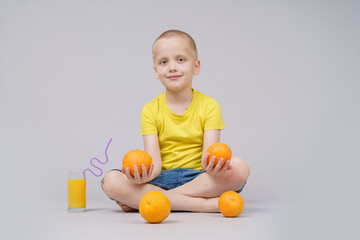 Smiling boy sitting with fruit orange and drink. Isolated on gray