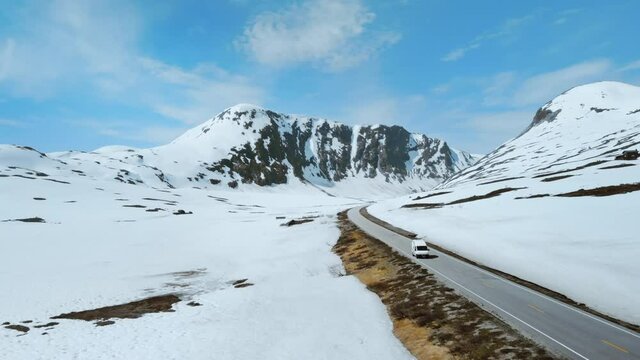 Cinematic drone shot of small RV camper van drive through epic mountain landscape of Norway. Beautiful concept of staycation vacation road trip through local country. Adventure freedom lifestyle 
