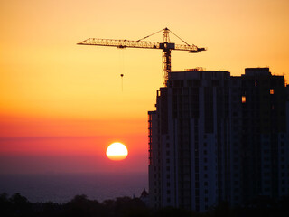 Construction site background. Silhouette of building under construction against the sea at sunrise. Self-erection crane.