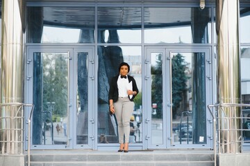 Pensive African American female lawyer in stylish formal suit holding folder with mock up area and looking away standing against courthouse. Half length of woman professional advocate with documents