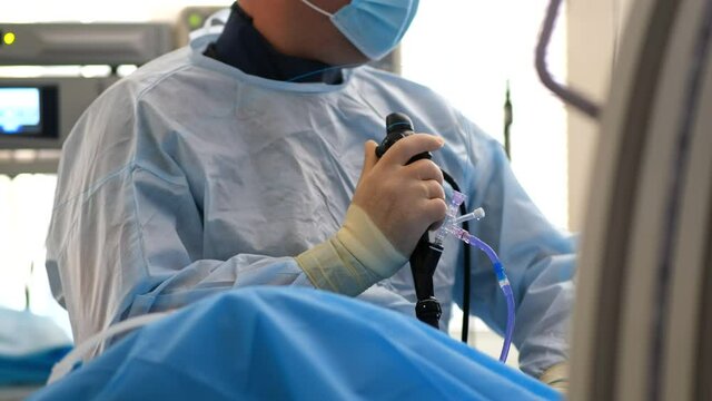 A doctor in a dressing gown, mask and rubber gloves performs a stone crushing operation in the operating room. Endoscopic surgery on the monitor.&nbsp;