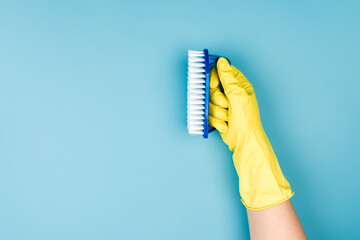 A hand in a yellow household glove holds a brush for cleaning furniture or the floor. 