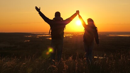 Travelers, man and a woman with backpack go to edge of mountain in rays of dawn, raise their hands in air and enjoy victory, beautiful sun and landscape. Free tourists travel. business teamwork