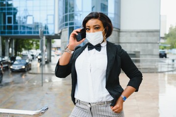 Fototapeta premium African American businesswoman wearing protective mask on her face in the city. The concept of visiting work during a pandemic