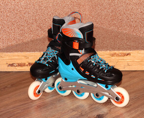 Roller skates on a wooden background. Roller skates are black and blue with orange color.