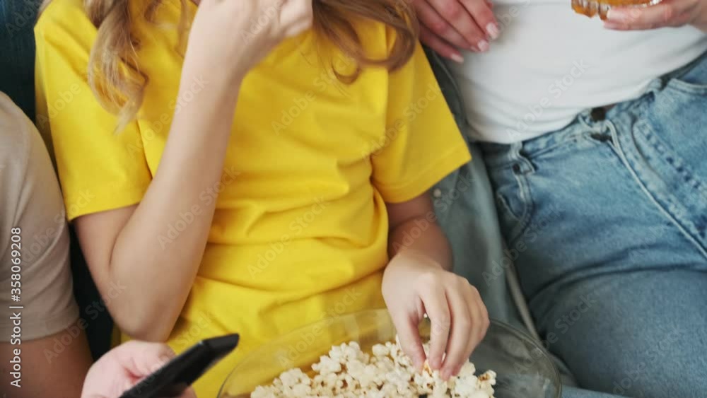 Wall mural a happy young family are eating popcorn while watching tv at home in the living room