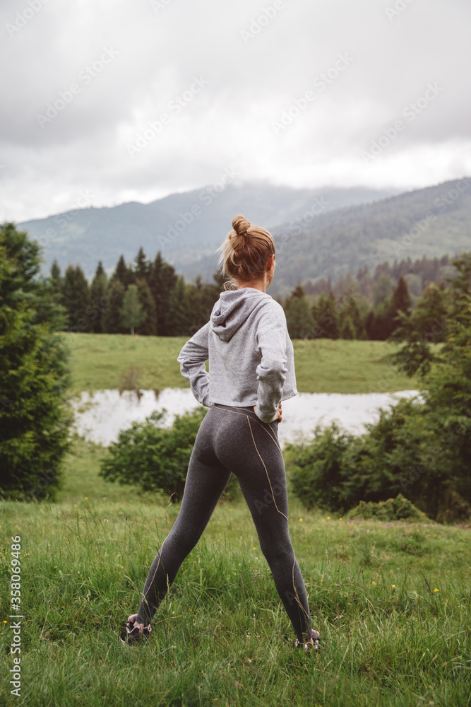 Wall mural young athletic runner female stretching in the forest before run. outdoor healthy lifestlye concept.