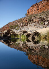 Fototapeta na wymiar Perfect reflection of orange rocky wall on still water. Green vegetation. No people. No clouds. Clean landscape. Vertical picture. Ormiston gorge, Macdonnell ranges, Northern Territory NT, Australia